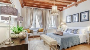 A bedroom with a wooden ceiling, a bed with a blue bedspread, a bench, a desk with a lamp, and a window with curtains. - Casa Arias in Lucca With 2 Bedrooms and 1 Bathrooms (Lucca)