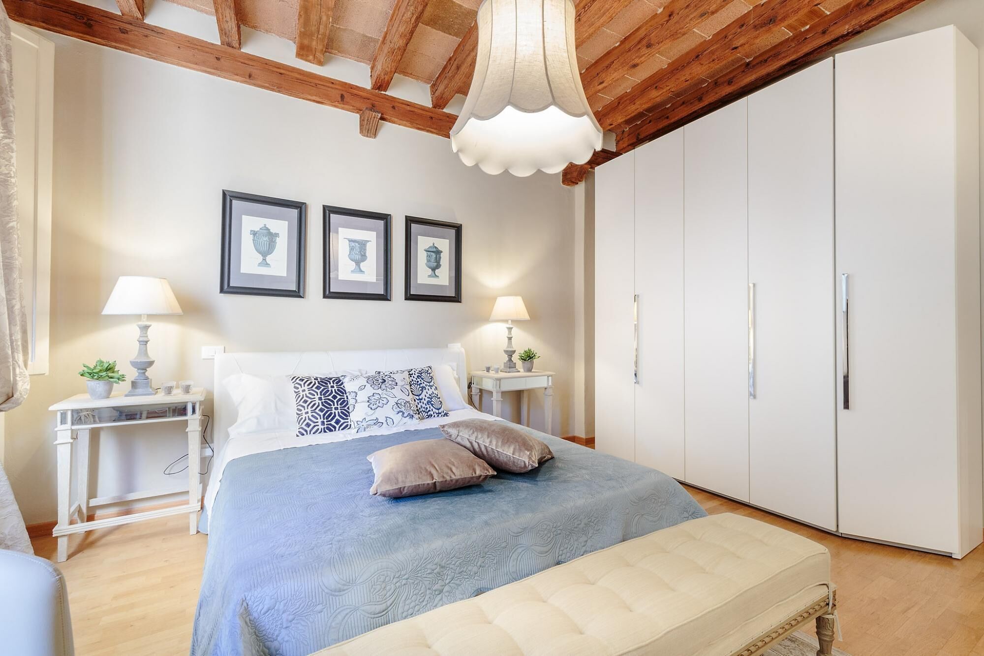 A bedroom with a bed, bedside tables, lamps, a wardrobe, and framed artwork on the wall.