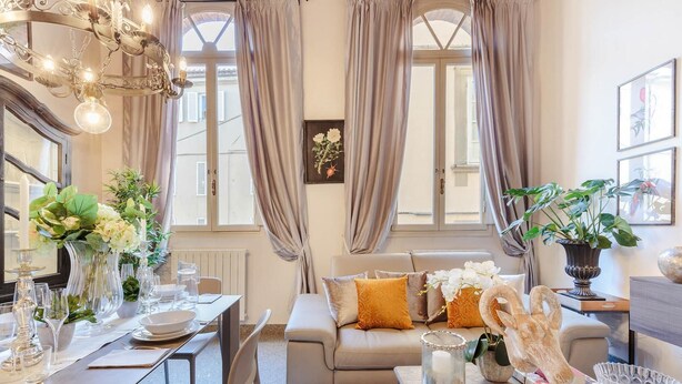 A well-lit living room with a dining area, featuring a sofa, dining table set with glassware, and various decorative items. - Casa Arias in Lucca With 2 Bedrooms and 1 Bathrooms (Lucca)