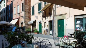 An outdoor cafe with tables and chairs, surrounded by buildings with green doors and shutters. - Casa Arias in Lucca With 2 Bedrooms and 1 Bathrooms (Lucca)