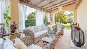 A cozy patio area with wicker furniture, a cushioned sofa, and a table with decorative items. - Villa Label in Camaiore (Camaiore)