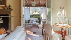 An open-plan living area with a fireplace, a dining table with a chandelier, and a view of a hillside. - Villa Label in Camaiore (Camaiore)