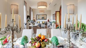 A dining area with a long table set for a meal, surrounded by ornate candelabras and a centerpiece of fruits and vegetables. - The Park View Apartment (Lucca)