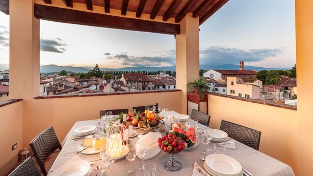 A balcony with a table set for dining, overlooking a cityscape with buildings and mountains. - The Park View Apartment (Lucca)