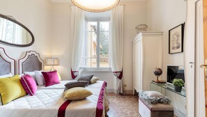 A bedroom with a bed, bedside table, lamp, and a window with curtains. - The Park View Apartment (Lucca)