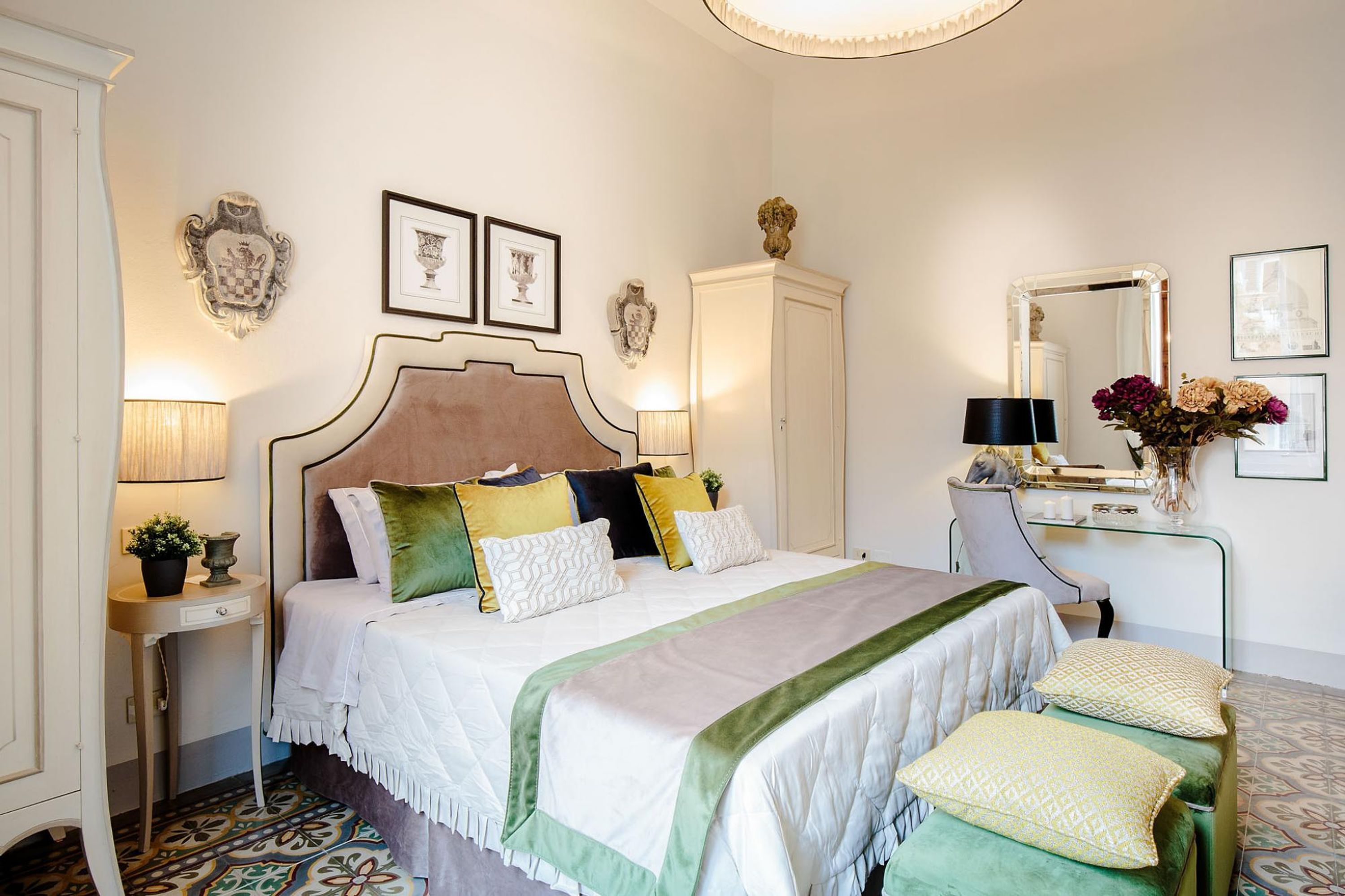 A neatly arranged bedroom with a bed, bedside tables, a desk, and a mirror.