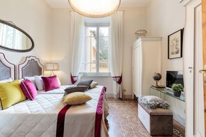 Un dormitorio con cama, mesita de noche, lámpara y ventana con cortinas.