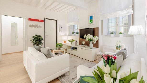 A modern living room with white sofas, a flat-screen TV, and a dining area with a white table and chairs.