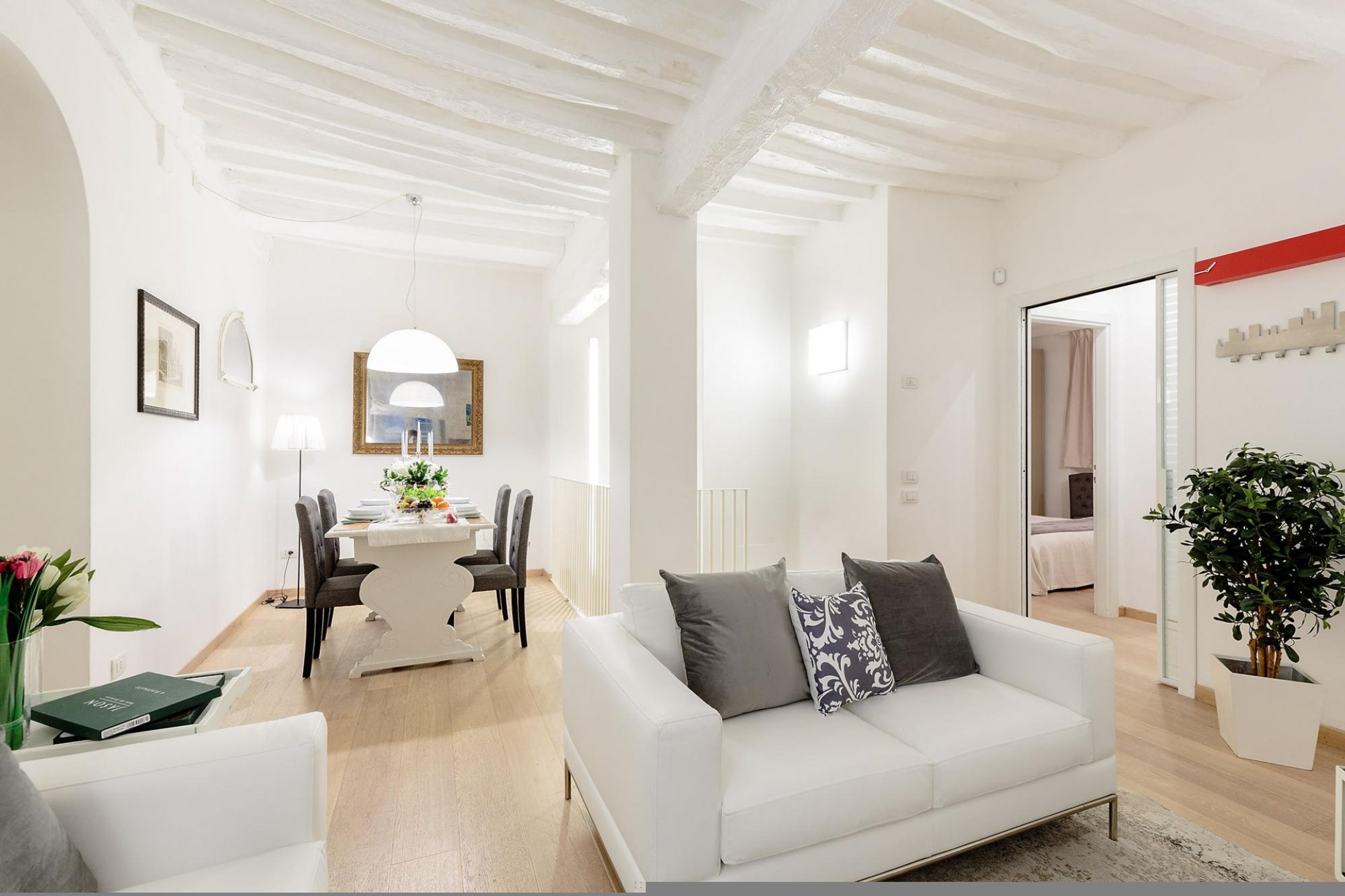 A modern living room with a white sofa, a dining area with a white table, and a kitchen visible through an open door.