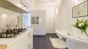 A modern kitchen with white cabinetry, a gas stove, and a stainless steel range hood. There is a white countertop with a vase of flowers and a glass pitcher.