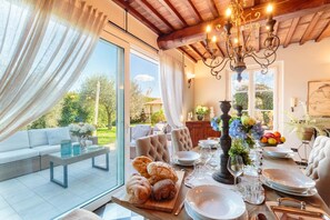 A dining area with a wooden table set for a meal, a sofa, and a view of the outdoors. - Villa Catia in Capannori (Capannori)