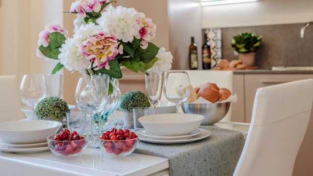 A dining table set with white plates, bowls, and a vase of flowers. - Casa Ugolino in Lucca (Lucca)