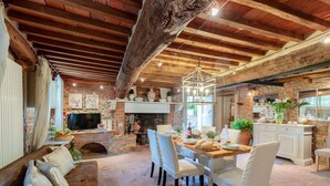 A rustic dining area with a wooden table, white chairs, and a brick fireplace. - Villa Hugo in Lucca With 5 Bedrooms and 6 Bathrooms (Lucca)