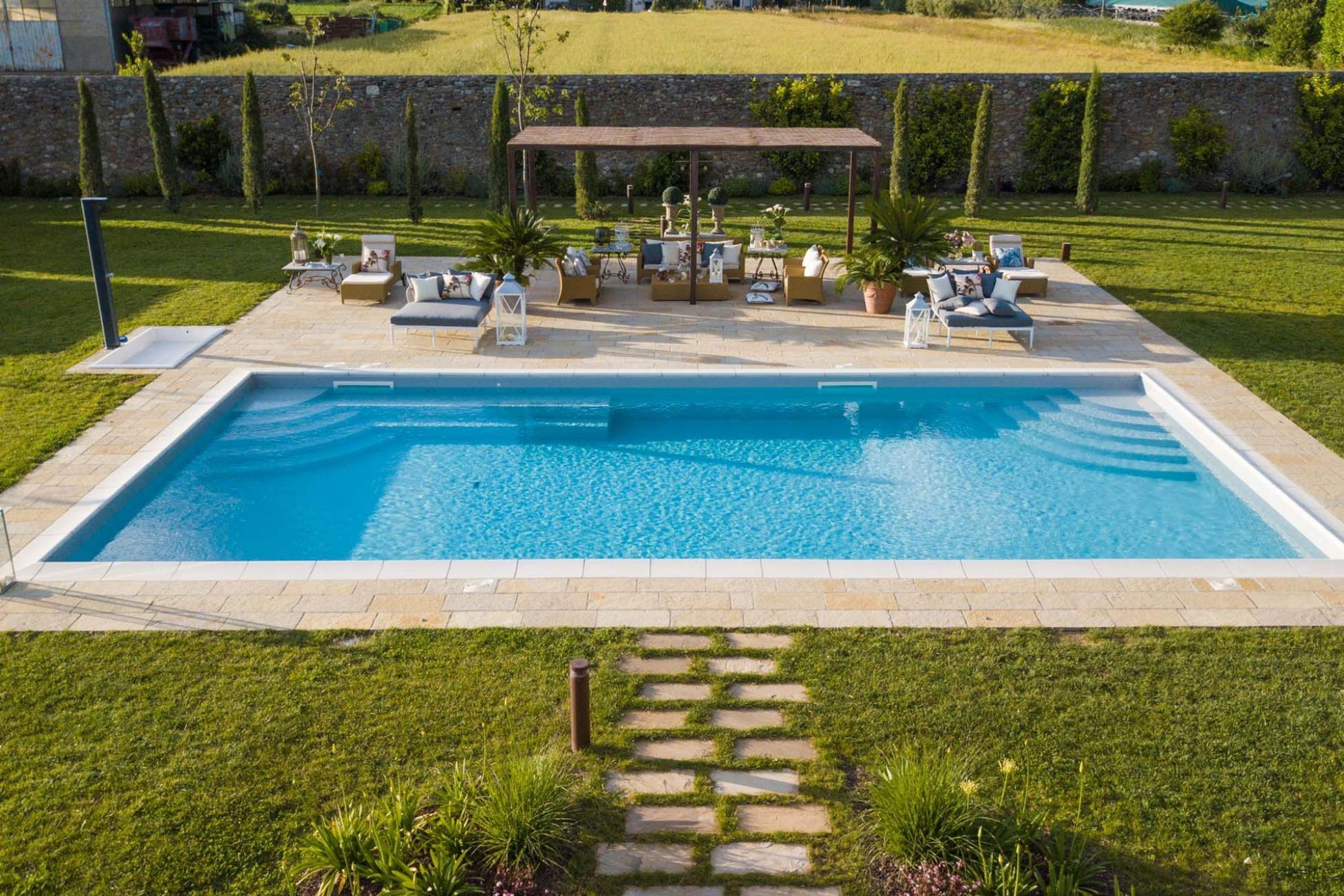 Piscina retangular com área de terraço, mobiliário de exterior e pérgula.