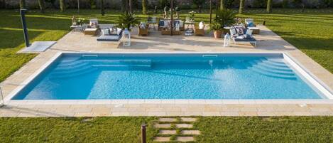 Piscina retangular com área de terraço, mobiliário de exterior e pérgula.