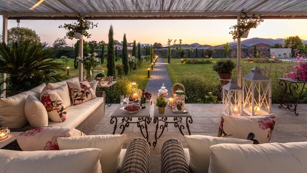 An outdoor seating area with wicker furniture and cushions, a pathway leading to a garden, and decorative lanterns. - Villa Hugo in Lucca With 5 Bedrooms and 6 Bathrooms (Lucca)