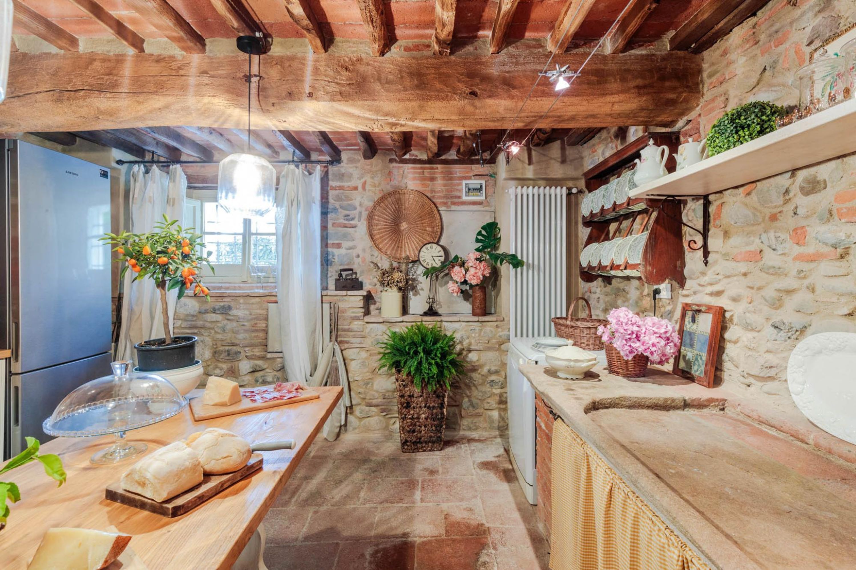 A rustic kitchen with exposed wooden beams, stone walls, and a variety of plants and kitchenware.