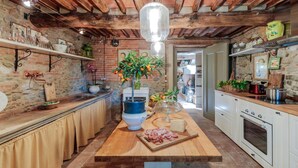 A rustic kitchen with exposed brick walls, wooden beams, and a central island with a vase of flowers, a cheese board, and a meat board. - Villa Hugo in Lucca With 5 Bedrooms and 6 Bathrooms (Lucca)