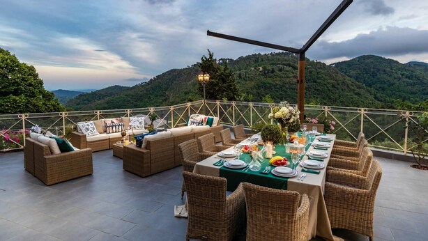 Un espace de restauration en plein air, avec des meubles en osier et une table dressée pour un repas, offrant une vue sur un paysage montagneux.