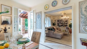 A dining area with a table set for four, a sofa in the background, and a chandelier in the living room. - Villa Dana in Segromigno in Monte (Capannori)