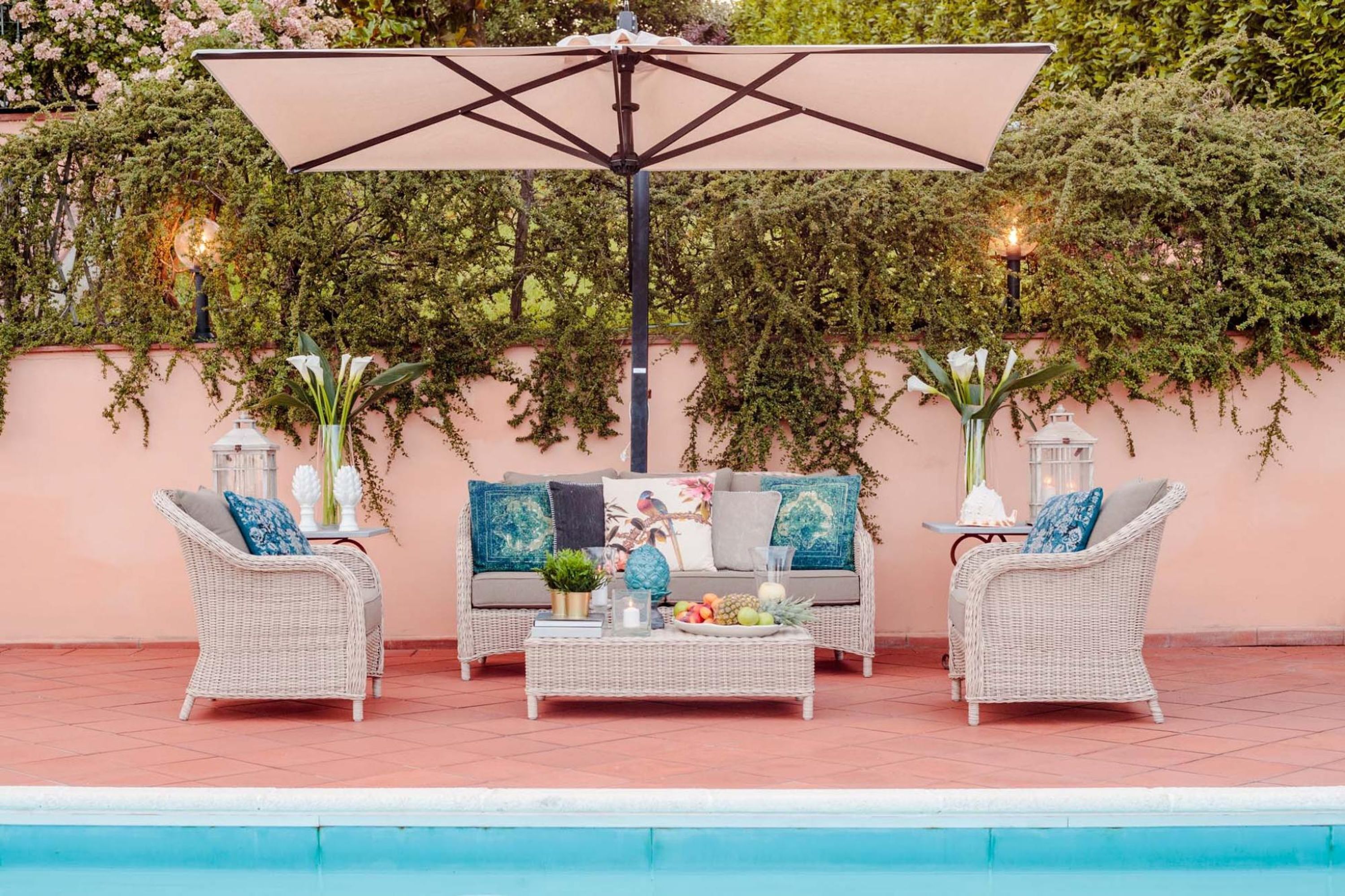An outdoor seating area with wicker furniture, a table with fruits and drinks, and a pool in the background.