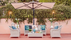 An outdoor seating area with wicker furniture, a table with fruits and drinks, and a pool in the background. - Villa Dana in Segromigno in Monte (Capannori)