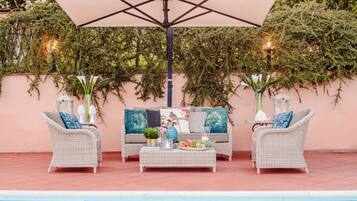 An outdoor seating area with wicker furniture, a table with fruits and drinks, and a pool in the background.