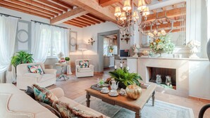 A spacious living room with a fireplace, wooden beams, and a chandelier. There are two sofas, a coffee table, and a dining table. - Villa Regina in Lucca (Lucca)