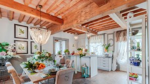 A dining area with a wooden table set for four, surrounded by chairs. There is a chandelier above the table, and the room has exposed wooden beams on the ceiling. - Villa Regina in Lucca (Lucca)