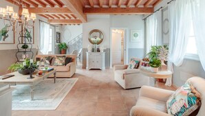 A spacious living room with a high ceiling, wooden beams, a chandelier, and a staircase leading to another level. - Villa Regina in Lucca (Lucca)