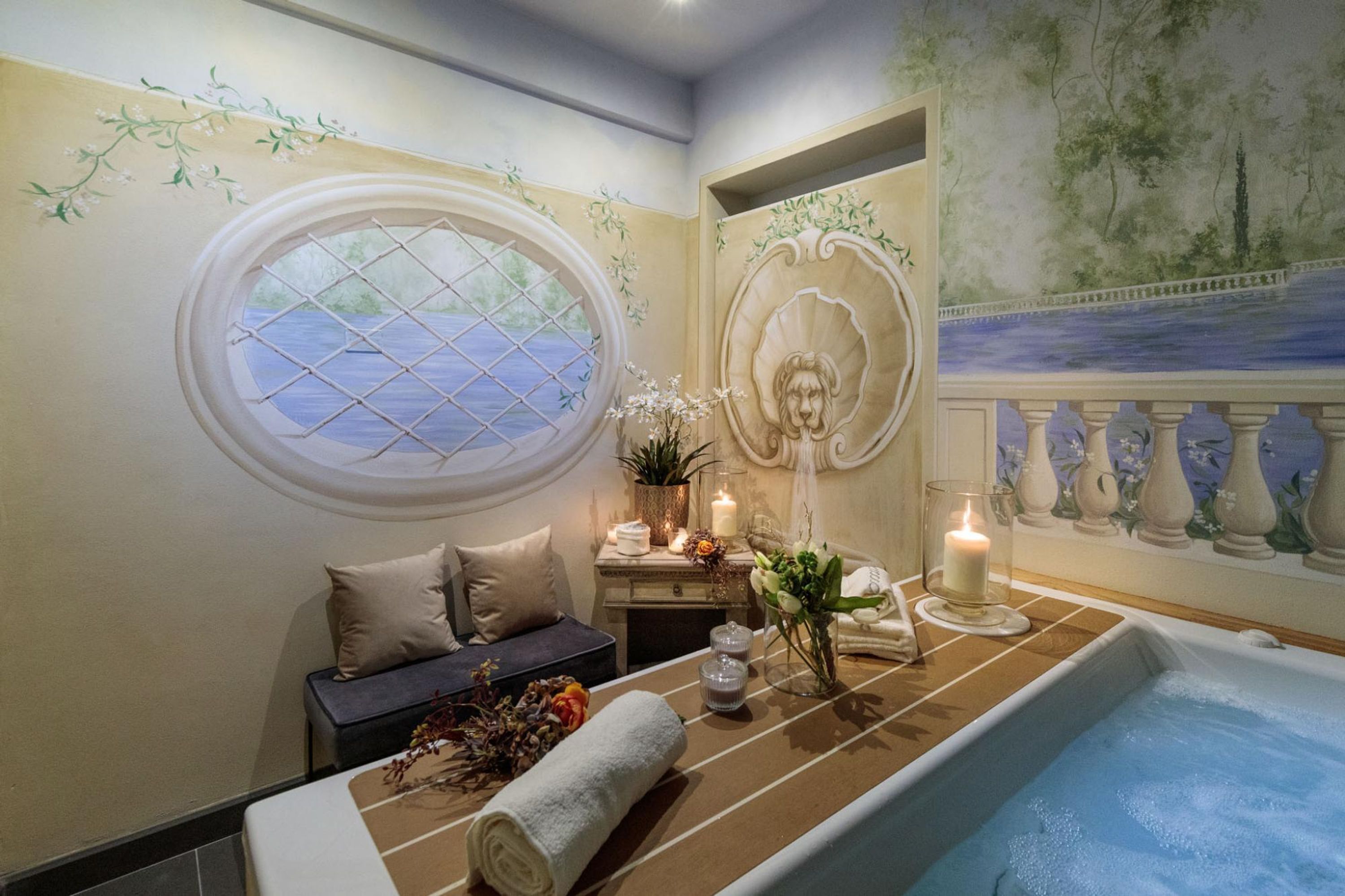 A spa room with a bathtub, a window with a view, decorative wall art, and a small table with candles and flowers.