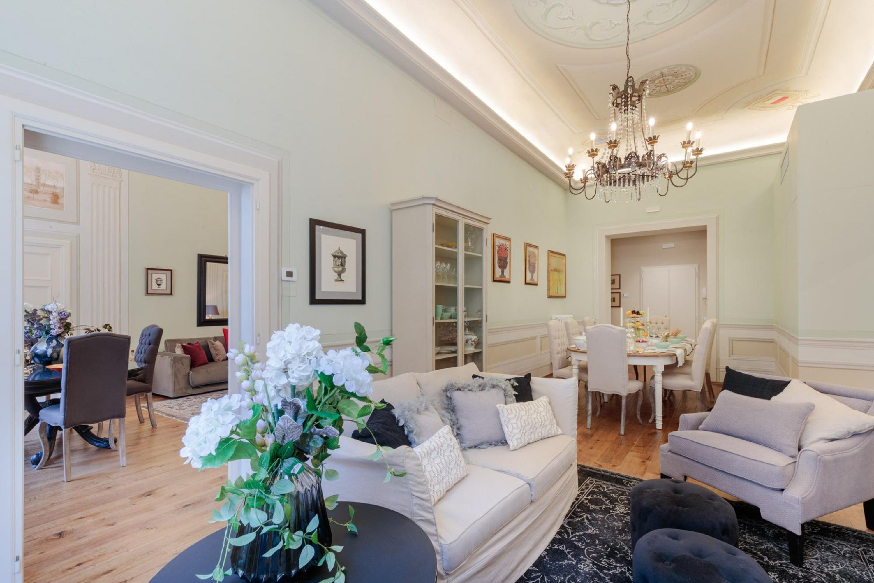 Ein geräumiges Wohnzimmer mit einem beige farbenen Sofa, einem schwarzen Ottomanen und einem Essbereich mit einem weißen Tisch und Stühlen.