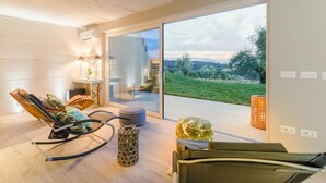 A modern room with a large sliding glass door leading to a balcony, a rocking chair, a small table with a lamp, and a wicker basket. - Villa Duemani - Pickleball Retreat (Capannori)