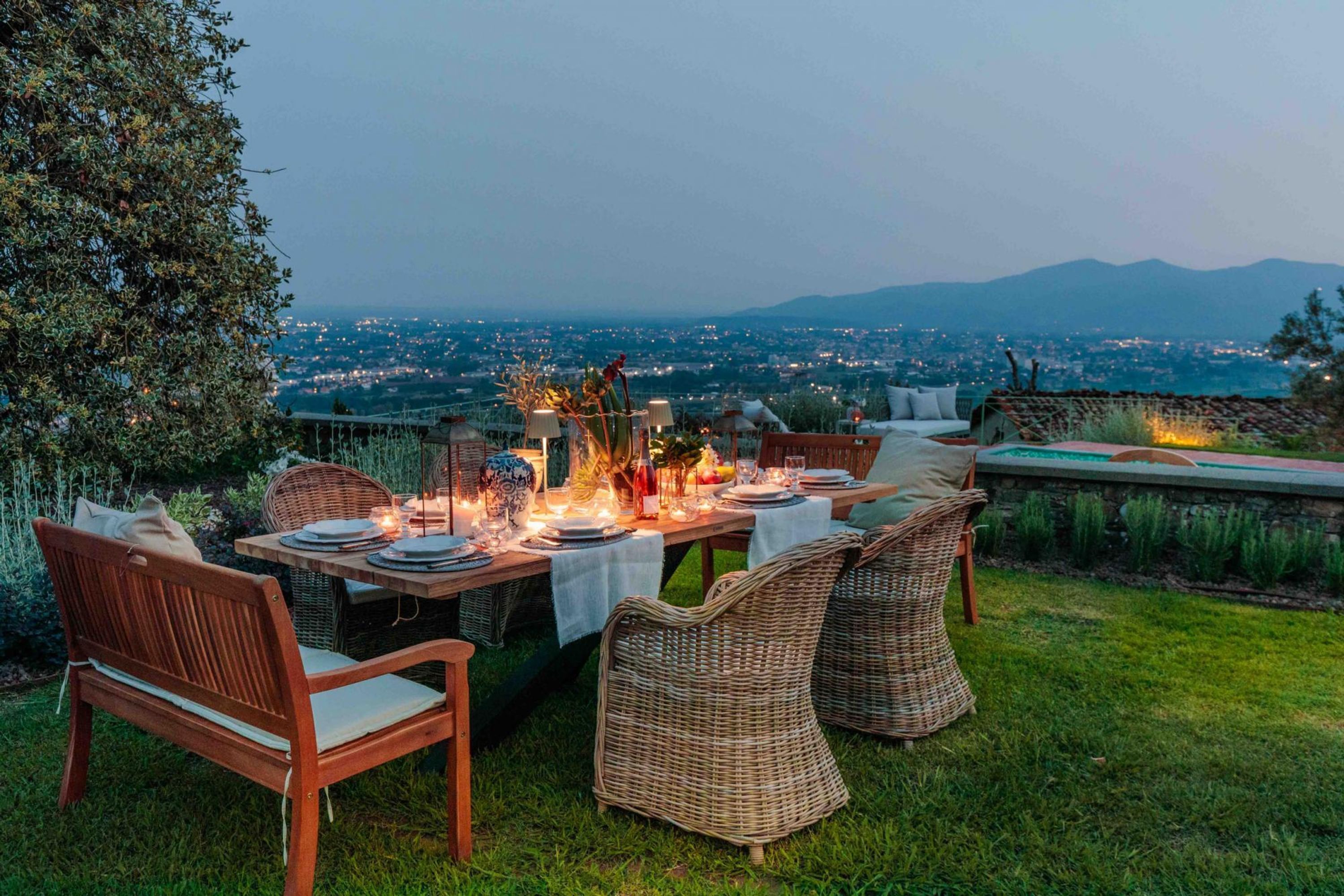 An outdoor dining area with wicker furniture, a table set for a meal, and a view of a cityscape and mountains in the background.