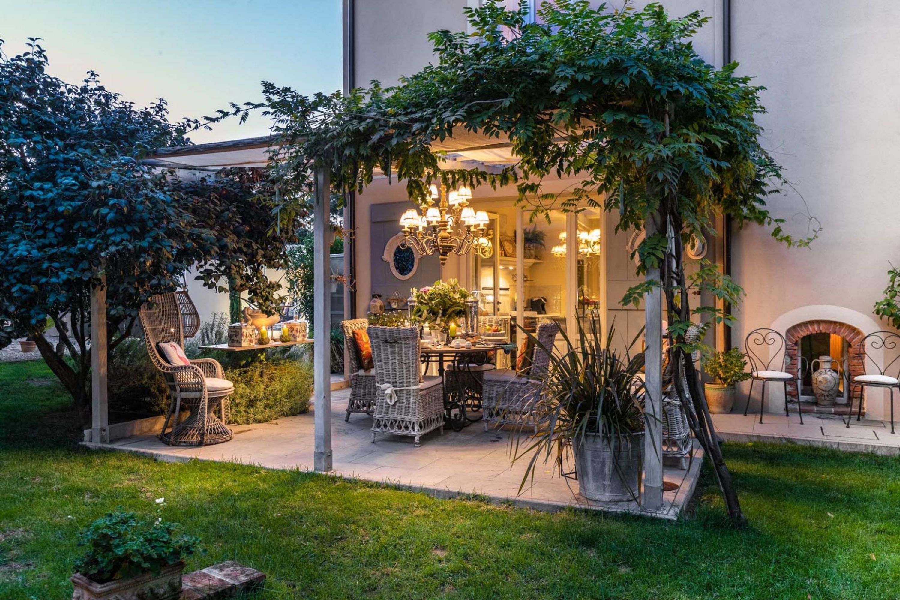 Un patio al aire libre con mobiliario de mimbre, una araña y una chimenea de ladrillo.