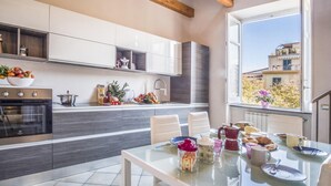 A modern kitchen with white cabinets, a built-in oven, and a dining area with a glass table. - Appartamento Caruso in Sorrento (Sorrento)
