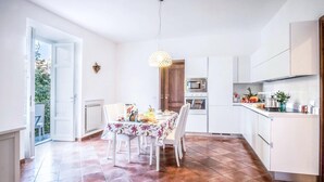 A modern kitchen with white cabinets, a dining table set for four, and a large window. - Maison Palazzo Correale (Sorrento)