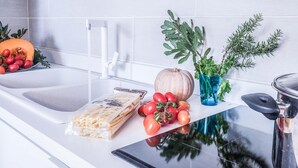 A kitchen counter with a white sink, a glass of water, a bowl of tomatoes, a pumpkin, and a bag of crackers. - Maison Palazzo Correale (Sorrento)