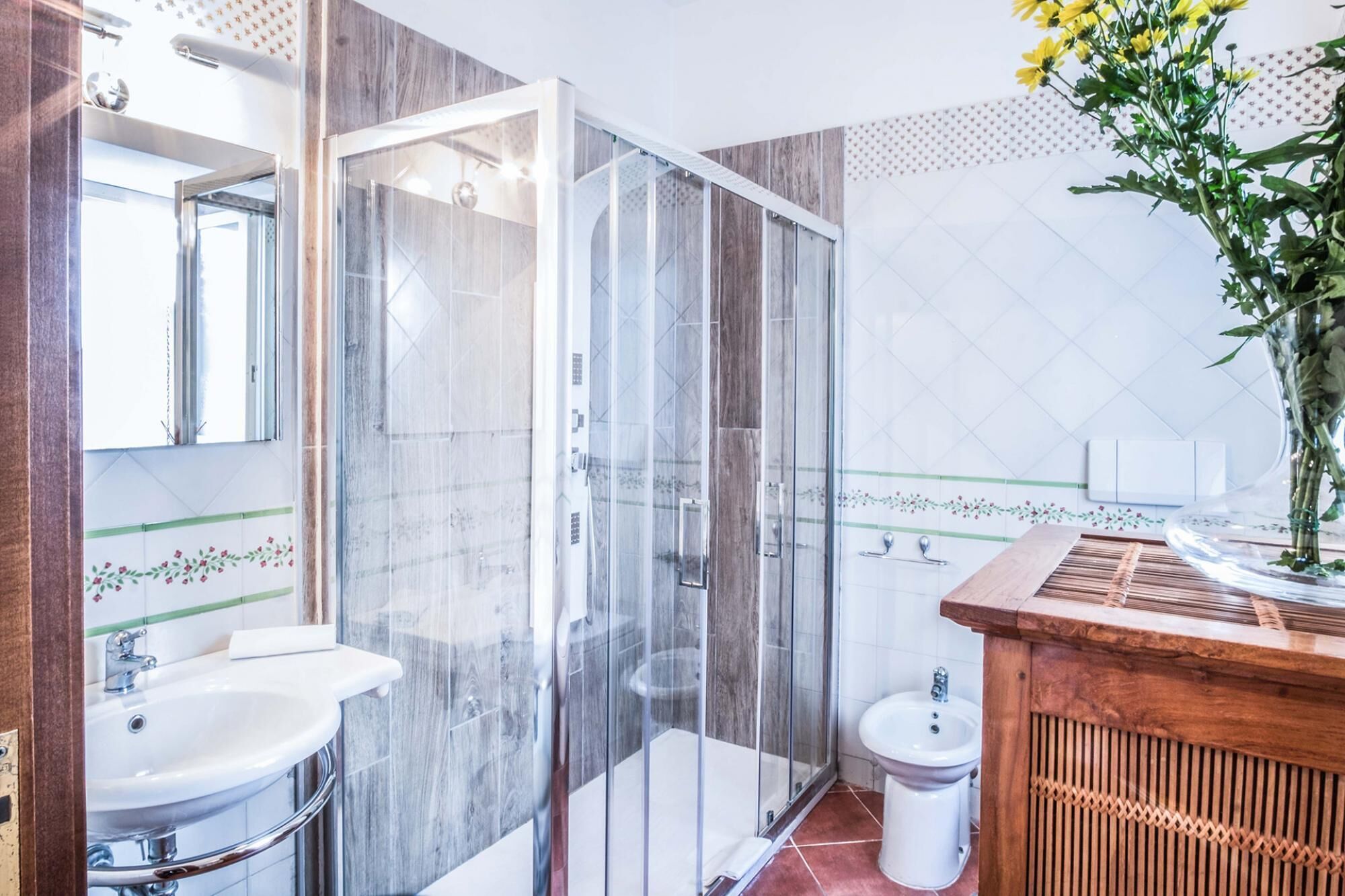 A bathroom with a glass-enclosed shower, a sink, a bidet, and a wooden vanity.