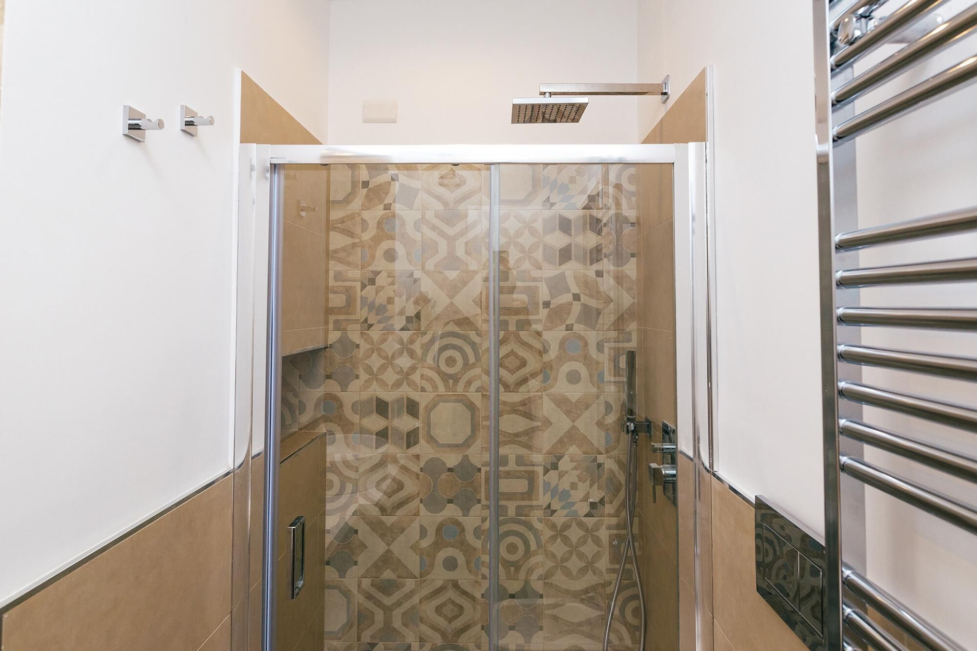 Un baño moderno con pared de ducha de diseño geométrico, una puerta de cristal y un perchero metálico.