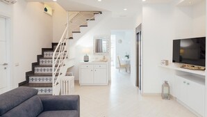 A modern living room with a grey sofa, a staircase with patterned tiles, a white cabinet, and a TV on a white shelf. - Villa Totti in Sant Agnello (Sant'Agnello)