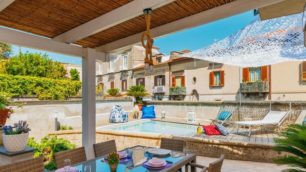 An outdoor pool area with lounge chairs, a dining table set for two, and a pergola overhead. - Villa Totti in Sant Agnello (Sant'Agnello)