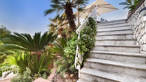 A staircase with stone steps leading up to a white railing, surrounded by lush greenery and palm trees. - Casa Augusta A in Sorrento (Sorrento)
