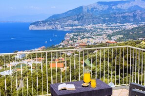 A balcony with a table, a book, a pitcher of orange juice, and a glass of juice. - Casa Augusta B in Sorrento (Sorrento)