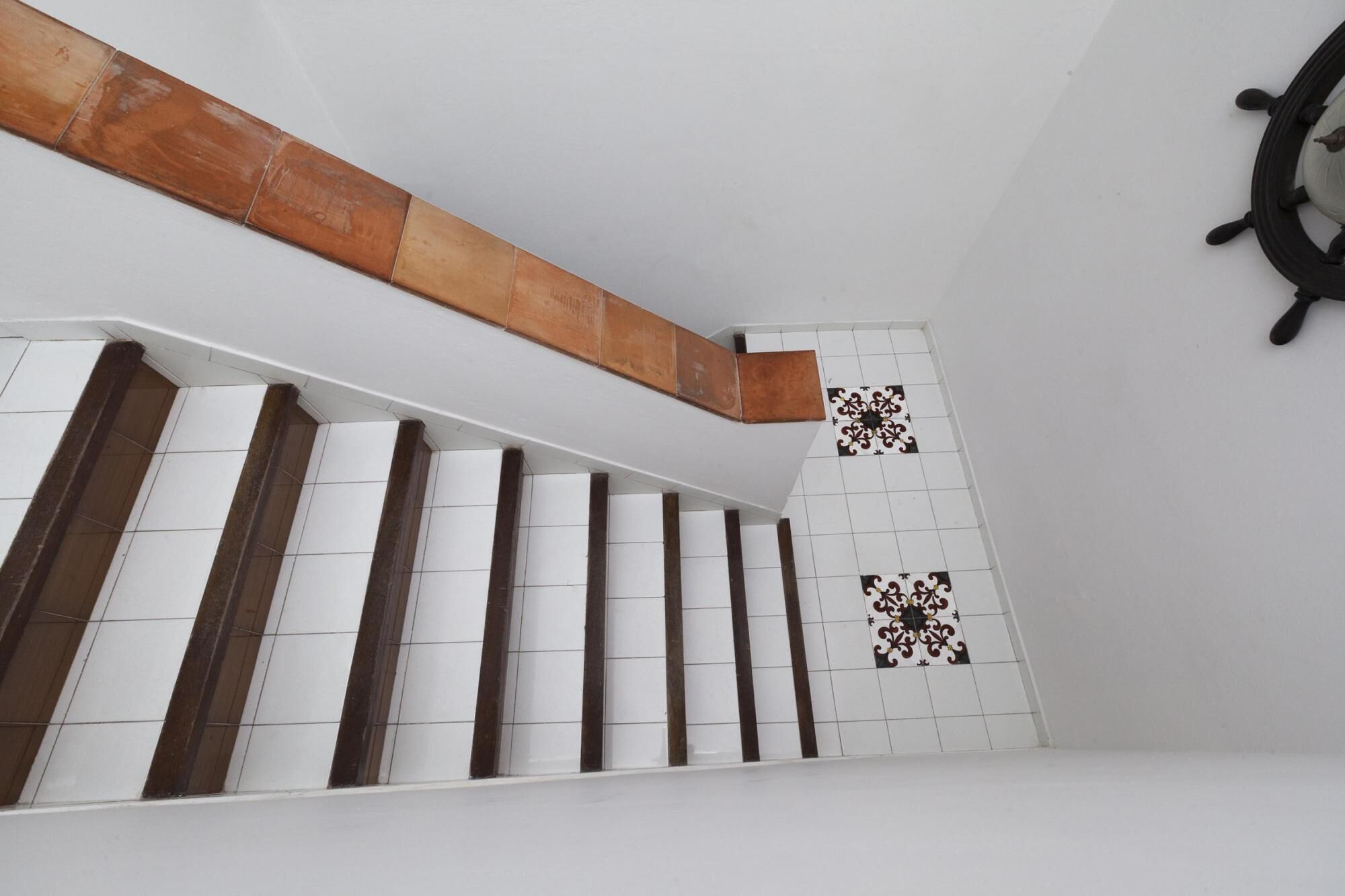 Eine Treppe mit weißen und braunen Fliesen, einem hölzernen Geländer und einem dekorativen Fliesendekor an der Wand.
