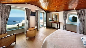 Une chambre spacieuse avec un grand lit, une chaise, un bureau et une fenêtre donnant sur la mer.