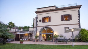 A two-story building with a patio area, outdoor seating, and a large arched entrance. - Residence Bosco - Villa Il Pino (Massa Lubrense)