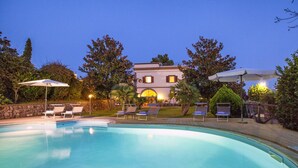 A swimming pool with lounge chairs and umbrellas, surrounded by trees and a building in the background. - Residence Bosco - Villa Il Pino (Massa Lubrense)