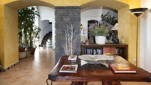 A spacious hallway with a wooden table, books, and potted plants. - Residence Bosco - Villa Il Pino (Massa Lubrense)