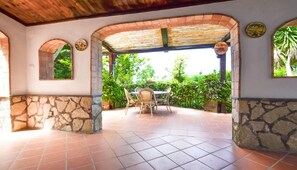 Un patio al aire libre con una pared de piedra, una mesa con sillas y una pérgola.